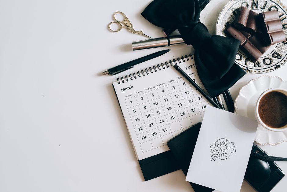 Flat lay of a desk with calendar, coffee, and chocolates. Elegant workspace setting.