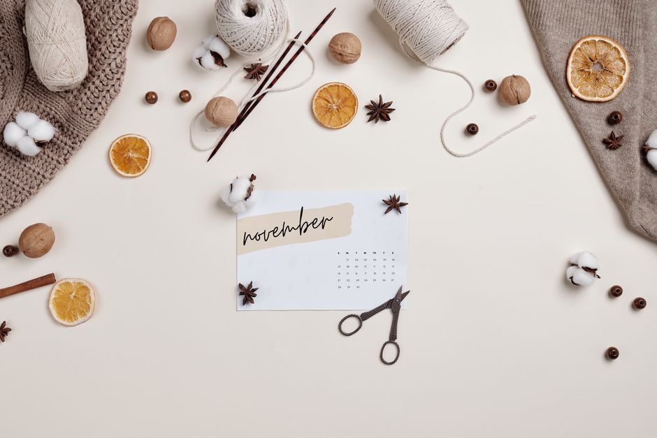 Flat lay of November calendar with cozy fall textiles, dried oranges, and knitting supplies.